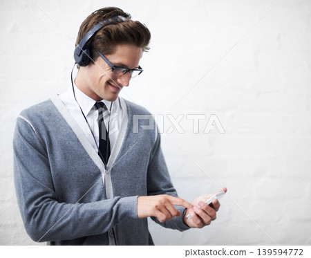 Man, headphones and listening to audio and phone for music by wall background, sound and peace. Male person, smartphone and streaming radio or podcast, online and hearing song and mobile application 139594772