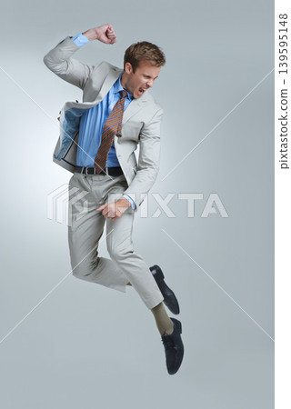 Businessman, celebration and jumping for success in studio, winner and fist pump for triumph. Male person, professional and victory or accomplishment, cheering and energy or bonus by gray background Businessman, celebration and jumping for success in studio, winner and fist pump for triumph. Male person, professional and victory or accomplishment, cheering and energy or bonus by gray background 139595148