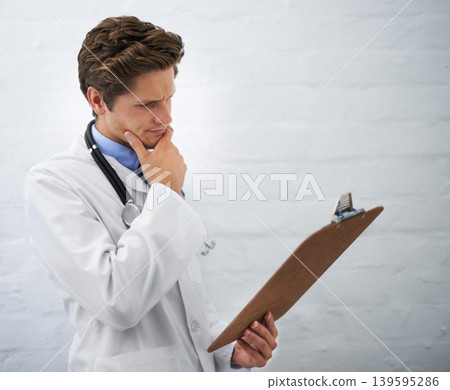 Clipboard, thinking and man doctor in office for reading or brainstorming for diagnosis treatment. Ideas, checklist and professional young male healthcare worker with decision face at hospital 139595286