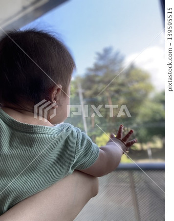 一個被抱著的嬰兒正把手伸出窗外。 139595515