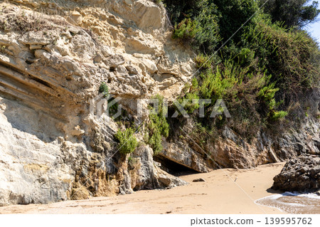 Rocky beach with vegetation and cave entrance under clear blue sky Rocky beach with vegetation and cave entrance under clear blue sky 139595762