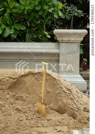 Pile of sand with a shovel in the foreground, set against a decorative Thai Buddhist temple fence in the background 139596625
