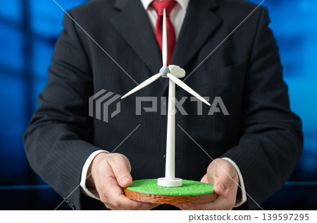 A businessman holds a wind turbine. Clean and green energy investments. Construction of new renewable energy facilities. Sustainable business development. 139597295