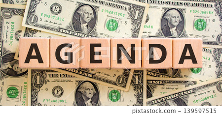 Agenda symbol. Concept word Agenda on beautiful wooden blocks. Beautiful dollar bills background. Beautiful dollar bills. Business agenda concept. Copy space. Agenda symbol. Concept word Agenda on beautiful wooden blocks. Beautiful dollar bills background. Beautiful dollar bills. Business agenda concept. Copy space. 139597515