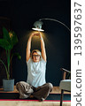 Middle aged woman on floor mat and doing stretching yoga position in modern Scandi dark interior home. Healthy Lifestyle. Sport activity for mature wellbeing. Mindful movement, relaxation. Vertical. 139597637