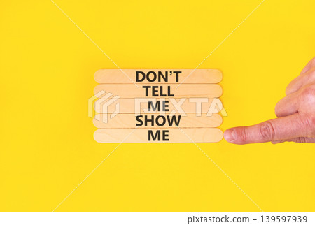 Tell or show symbol. Concept words Do not tell me, show me on beautiful wooden sticks. Beautiful yellow paper background. Businessman hand. Business tell or show concept. Copy space. Tell or show symbol. Concept words Do not tell me, show me on beautiful wooden sticks. Beautiful yellow paper background. Businessman hand. Business tell or show concept. Copy space. 139597939