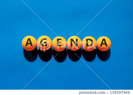 Agenda symbol. Concept word Agenda on beautiful orange table tennis ping pong balls. Beautiful blue background. Business agenda concept. Copy space. Agenda symbol. Concept word Agenda on beautiful orange table tennis ping pong balls. Beautiful blue background. Business agenda concept. Copy space. 139597949