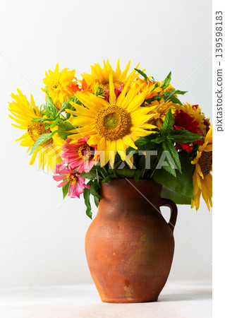 Flowers in a vase fill a space with color and texture. Sunflowers, zinnias, and greenery are mixed together. Light brightens the scene, showcasing their vibrant colors Flowers in a vase fill a space with color and texture. Sunflowers, zinnias, and greenery are mixed together. Light brightens the scene, showcasing their vibrant colors 139598183