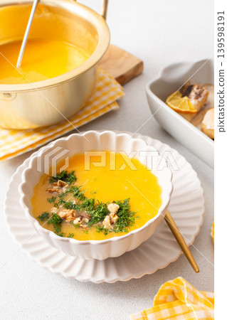 Pumpkin cream soup sits in a bowl with toppings next to a dish of baked hake and lemon. A spoon rests beside the soup in a clean dining area Pumpkin cream soup sits in a bowl with toppings next to a dish of baked hake and lemon. A spoon rests beside the soup in a clean dining area 139598191