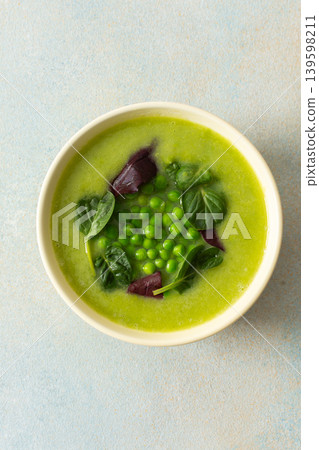 Bright green soup made with broccoli and green peas sits in a bowl. The meal includes liver pate and grissini, suitable for breakfast or lunch 139598211