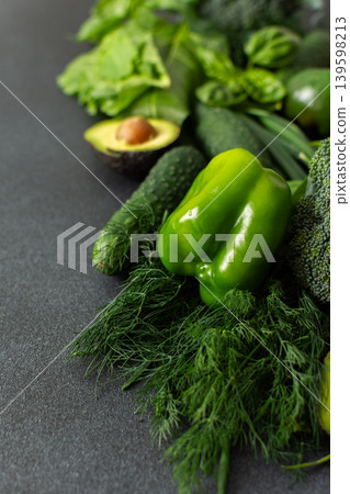 A vibrant assortment of fresh green vegetables is carefully arranged on a dark surface. This selection includes broccoli, green bell peppers, cucumbers, spinach, lettuce, and an avocado A vibrant assortment of fresh green vegetables is carefully arranged on a dark surface. This selection includes broccoli, green bell peppers, cucumbers, spinach, lettuce, and an avocado 139598213