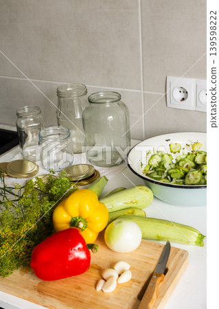 Cucumbers, peppers, and zucchini are being prepared and placed in jars for canning. Fresh ingredients are cut and organized on a clean kitchen counter for preserving Cucumbers, peppers, and zucchini are being prepared and placed in jars for canning. Fresh ingredients are cut and organized on a clean kitchen counter for preserving 139598222