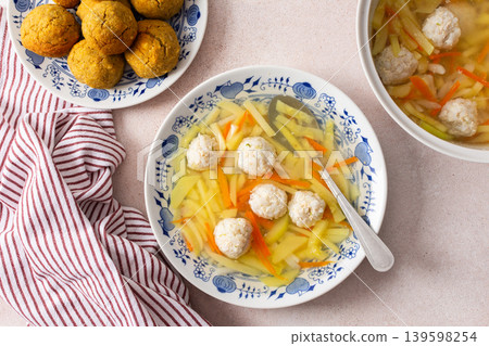 A bowl of vegetable soup with chicken meatballs is served alongside chickpea buns on a table. Fresh ingredients create a hearty meal for breakfast or lunch A bowl of vegetable soup with chicken meatballs is served alongside chickpea buns on a table. Fresh ingredients create a hearty meal for breakfast or lunch 139598254