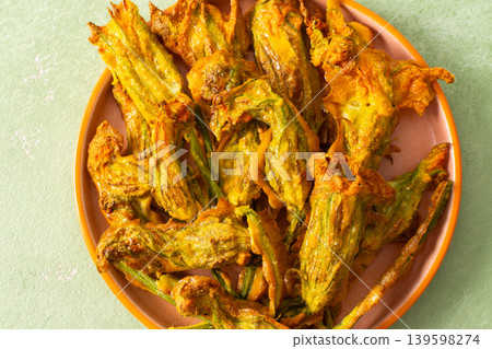 Crispy deep-fried zucchini flowers are displayed on a vibrant plate, showcasing their golden texture. Perfect for sharing during a summer gathering or family meal Crispy deep-fried zucchini flowers are displayed on a vibrant plate, showcasing their golden texture. Perfect for sharing during a summer gathering or family meal 139598274