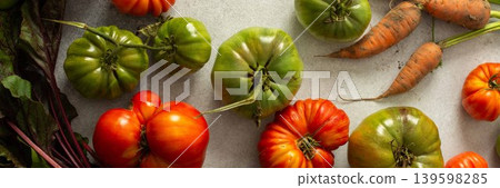 Various types of tomatoes and carrots are placed together on a flat surface. The assortment shows green and ripe tomatoes along with leafy greens and roots, banner Various types of tomatoes and carrots are placed together on a flat surface. The assortment shows green and ripe tomatoes along with leafy greens and roots, banner 139598285