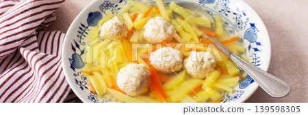 A bowl filled with vegetable soup featuring chicken meatballs sits on a surface with a striped cloth nearby. This dish is ideal for any meal during the day, banner A bowl filled with vegetable soup featuring chicken meatballs sits on a surface with a striped cloth nearby. This dish is ideal for any meal during the day, banner 139598305