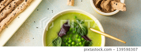 A bowl of creamy broccoli and green pea soup sits on a green plate. Next to it is liver pate in a small dish and grissini on a white platter. This meal provides healthy options, banner A bowl of creamy broccoli and green pea soup sits on a green plate. Next to it is liver pate in a small dish and grissini on a white platter. This meal provides healthy options, banner 139598307