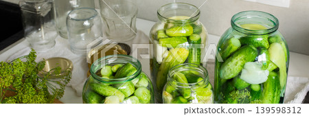Cucumbers are being prepared and placed into glass jars for canning in a kitchen. The process helps preserve cucumbers for winter use, ensuring they last longer, banner Cucumbers are being prepared and placed into glass jars for canning in a kitchen. The process helps preserve cucumbers for winter use, ensuring they last longer, banner 139598312
