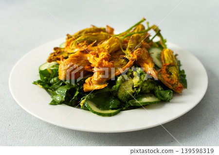 Roasted zucchini flowers sit on a bed of salad made with fresh greens, cucumbers, and broccoli. This dish highlights summer flavors and healthy eating options Roasted zucchini flowers sit on a bed of salad made with fresh greens, cucumbers, and broccoli. This dish highlights summer flavors and healthy eating options 139598319