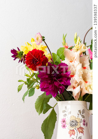 A vase holds a variety of fresh flowers with different colors. The flowers are placed on a pink table. Behind the vase is a plain wall in a bright room A vase holds a variety of fresh flowers with different colors. The flowers are placed on a pink table. Behind the vase is a plain wall in a bright room 139598337