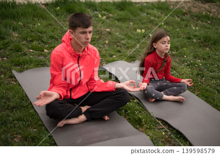Enjoying peaceful moments in nature during a tranquil afternoon, we find children happily practicing mindfulness while sitting in the grass Enjoying peaceful moments in nature during a tranquil afternoon, we find children happily practicing mindfulness while sitting in the grass 139598579