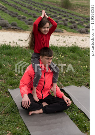 Mindful moments in a serene lavender field with a child perched playfully on an adult's shoulders during a tranquil yoga session on a sunny day 139598583