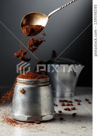 Grounded coffee is poured into a classic Italian aluminium moka pot, models from the 1950s to the 1960s. Grounded coffee is poured into a classic Italian aluminium moka pot, models from the 1950s to the 1960s. 139598595