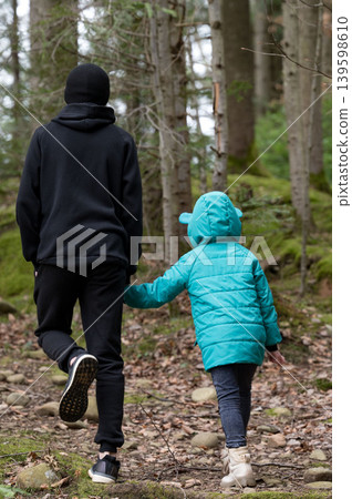 Walking hand in hand through a tranquil forest trail on a cool autumn day, a child and an older companion embrace nature's beauty and togetherness Walking hand in hand through a tranquil forest trail on a cool autumn day, a child and an older companion embrace nature's beauty and togetherness 139598610