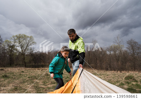 The family comes together, sharing laughter and smiles, as they set up a tent in a vibrant meadow filled with blooming flowers. 139598661