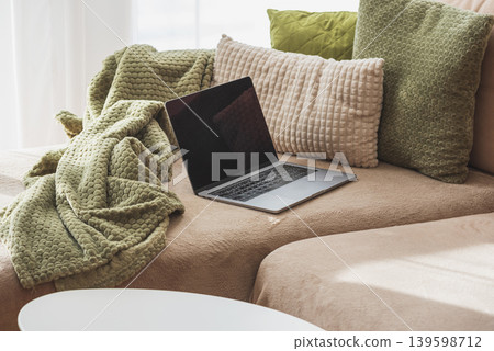 Laptop on Cozy Sofa with Textured Pillows and Blanket. Relaxed Home Workspace Laptop on Cozy Sofa with Textured Pillows and Blanket. Relaxed Home Workspace 139598712