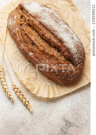 Rye bread loaf with wheat ears on parchment paper 139598812