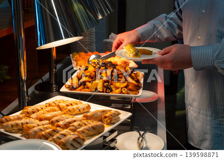 Person serving hot dishes at a hotel buffet with tongs 139598871