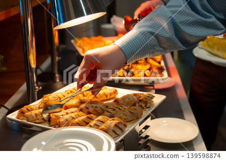 Hand using tongs to serve grilled chicken rolls with sauce at a hot hotel buffet Hand using tongs to serve grilled chicken rolls with sauce at a hot hotel buffet 139598874