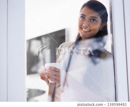 Window, woman and coffee with thinking, idea and morning drink at home with a smile. Daydreaming, tea and relax Indian female person in a house lounge with peace, calm and happy in a living room Window, woman and coffee with thinking, idea and morning drink at home with a smile. Daydreaming, tea and relax Indian female person in a house lounge with peace, calm and happy in a living room 139599481