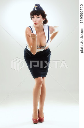 Portrait, blowing kiss and woman flight attendant in studio on gray background for vintage fashion. Travel, model and pin up with confident young air hostess in work uniform for retro service 139599720