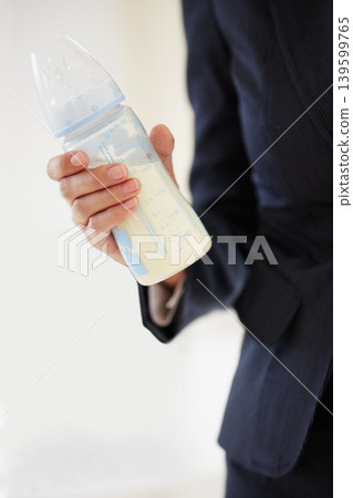Business, woman and mom with baby bottle in suit, working and balance a career with motherhood. Hand, closeup and mother with milk in container for child, care and management of family with a job Business, woman and mom with baby bottle in suit, working and balance a career with motherhood. Hand, closeup and mother with milk in container for child, care and management of family with a job 139599765