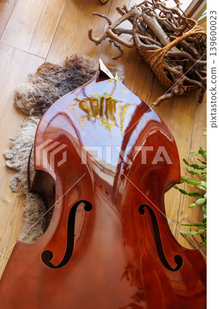 Damaged contrabass body lying on a wooden floor near a window, with the neck broken off after a fall. Cassical string instrument repair concept Damaged contrabass body lying on a wooden floor near a window, with the neck broken off after a fall. Cassical string instrument repair concept 139600023