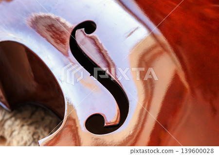 Contrabass body with f hole on glossy varnished wood close up. Double bass texture with reflections. Classical string instrument detail Contrabass body with f hole on glossy varnished wood close up. Double bass texture with reflections. Classical string instrument detail 139600028