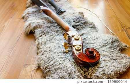 Broken contrabass neck joint with fingerboard, headstock with scroll, pegbox, tuning keys, nuts, pegs and brass plates lying on the wooden floor on felted wool locks rug.Copy space 139600044