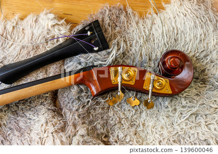 Detached contrabass neck joint with fingerboard, tailpiece and scroll with pegbox on felted wool locks blanket. Top view Detached contrabass neck joint with fingerboard, tailpiece and scroll with pegbox on felted wool locks blanket. Top view 139600046