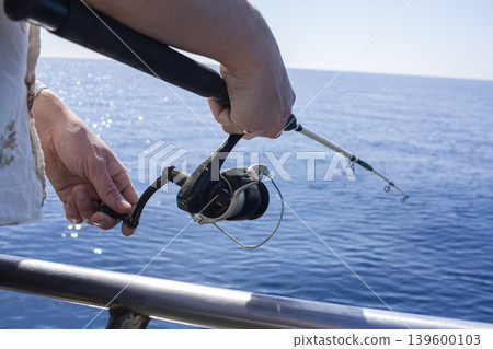 Close-up of man's hand holding fishing rod in the sea, man fishing. Fishing rod with a spinning reel in the hands of a fisherman. Close-up of man's hand holding fishing rod in the sea, man fishing. Fishing rod with a spinning reel in the hands of a fisherman. 139600103