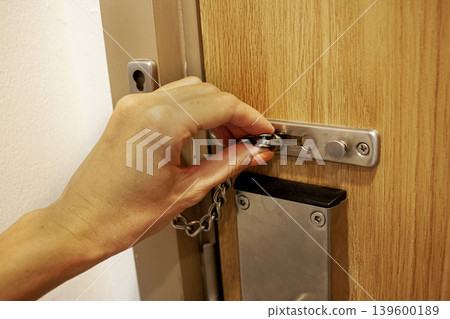 Safety lock. Hand closes the door close-up. Safety Chain Door Lock Safety lock. Hand closes the door close-up. Safety Chain Door Lock 139600189