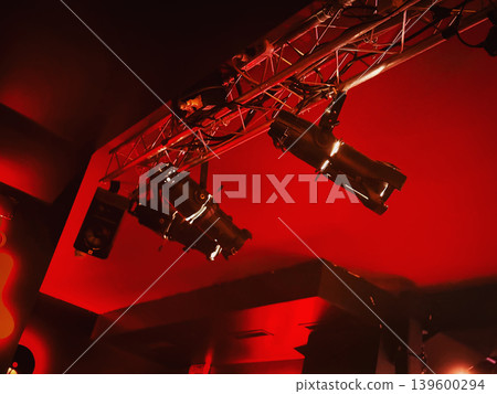 Stage lighting hangs from metal truss above concert venue, with spotlights, rigging, cables, red illumination. Concept of stage lighting design, event production, show setup, performance tech 139600294