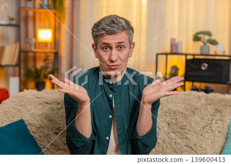Young man lifts hands in air and looks confused reacting to unexpected situation or sudden question Young man lifts hands in air and looks confused reacting to unexpected situation or sudden question 139600413