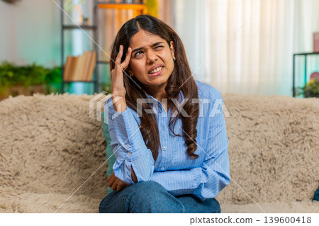 Indian woman touching head with tension and pain from headache at home, exhausted and uncomfortable Indian woman touching head with tension and pain from headache at home, exhausted and uncomfortable 139600418