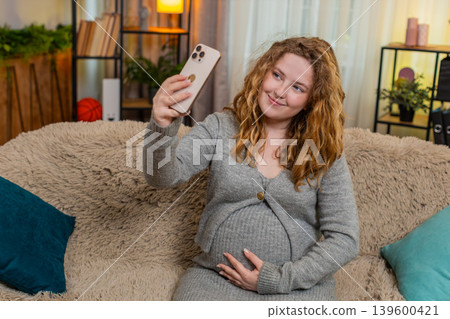 Pregnant woman taking selfie with baby bump on smartphone smiling gently touching belly at home Pregnant woman taking selfie with baby bump on smartphone smiling gently touching belly at home 139600421