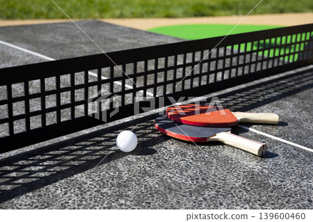 Table tennis rackets close-up. Ping pong rackets and ball on a public table in city park Table tennis rackets close-up. Ping pong rackets and ball on a public table in city park 139600460