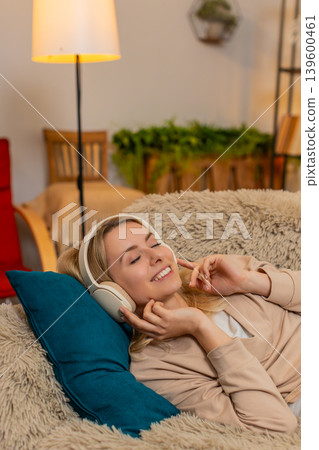 Woman lying on couch with eyes closed, listening to music through headphones in peaceful relaxation Woman lying on couch with eyes closed, listening to music through headphones in peaceful relaxation 139600461