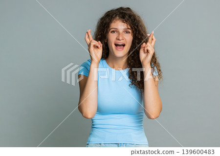 Young woman smiling crossing fingers hoping good luck wish positive optimistic anticipation gesture Young woman smiling crossing fingers hoping good luck wish positive optimistic anticipation gesture 139600483