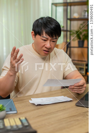 Asian man throwing bills onto table after shocking amount, eyebrows raised, very frustrated reaction Asian man throwing bills onto table after shocking amount, eyebrows raised, very frustrated reaction 139600491